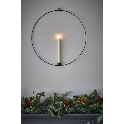 Candle in a black wall mounted ring above a mantel with a christmas wreath 