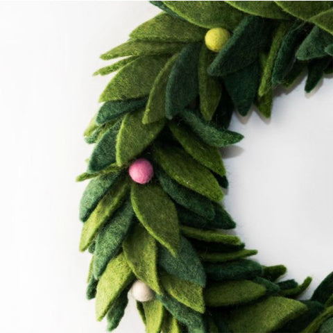 A green felt Christmas wreath with layered leaf details, small colorful pom-pom ornaments in red, pink, yellow, and white, and a white hanging loop at the top, shown on a plain white background.
