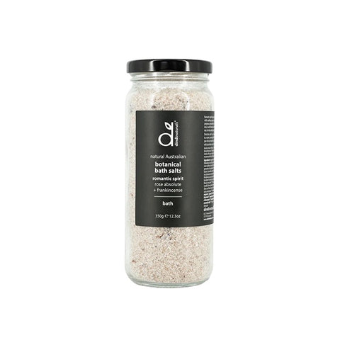Jar of bath salts with a label on a white surface with candles and flowers in the background