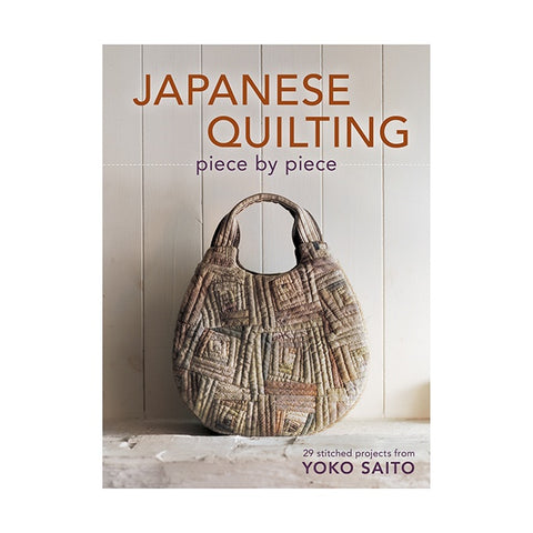 Book cover of 'Japanese Quilting piece by piece' with a textured bag on a wooden background