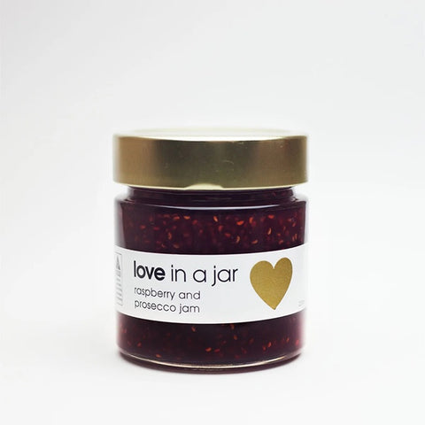 Jar of raspberry and prosecco jam with a gold lid on a white background
