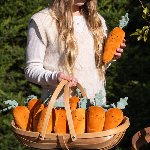 A plush carrot toy with a smiling face, featuring an orange body and green corduroy-style leaves, photographed on a clean white background.