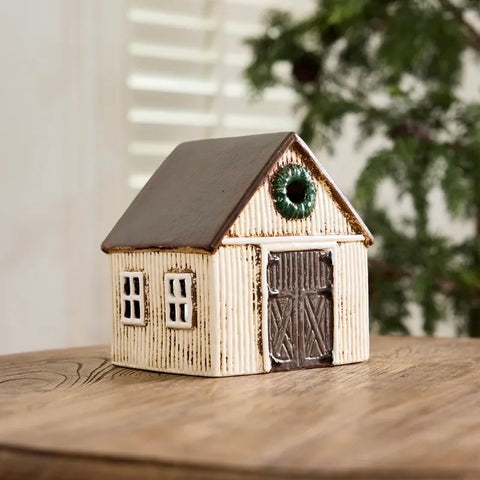 A small decorative barn-shaped birdhouse with a distressed cream-colored exterior, dark brown roof, and a green circular accent near the peak, shown on a light gray background.