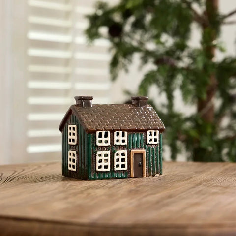 A miniature decorative house figurine with green painted siding, a brown shingled roof, white window frames, and a brown door, shown on a plain light gray background.