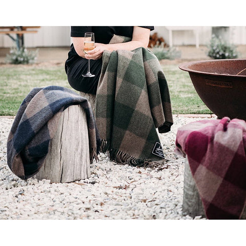 The Grampian Goods Co Wool Check Blanket Antipodean Collection in Cypress hangs on a ladder by a fence