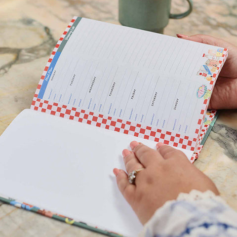 Hand holding a colorful notebook titled 'The Stress Free Kitchen Kit' with decorative elements by Write to Me