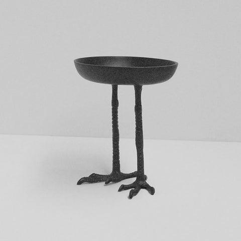 Gold bird-shaped jewelry stand on a wooden surface with books and a plant in the background.
