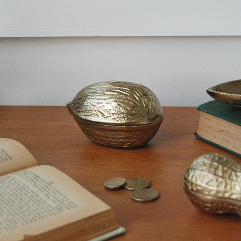 Decorative metal nutshells on a wooden surface with books and coins.